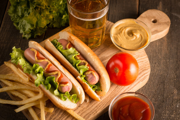 烧烤热狗的照片，在木制背景上涂上黄色芥末和番茄酱。热狗三明治配土豆薯条和酱汁。图片下载