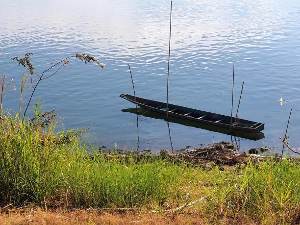 一艘船漂浮在草地岸边的水面上的照片。图片下载