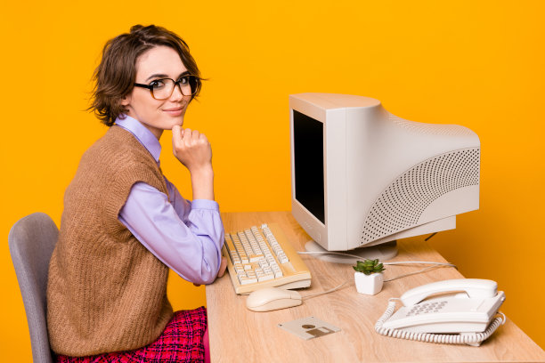 照片肖像的迷人的年轻女子工作过程中，旧电脑穿着复古的办公服装孤立在黄色的背景图片下载