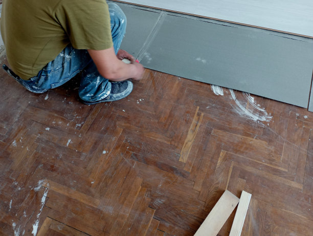 照片中，工匠正在修补房间的地板，并在木质拼花地板上铺设柔软的床上用品，以便铺设层压板。修理的话题。图片下载