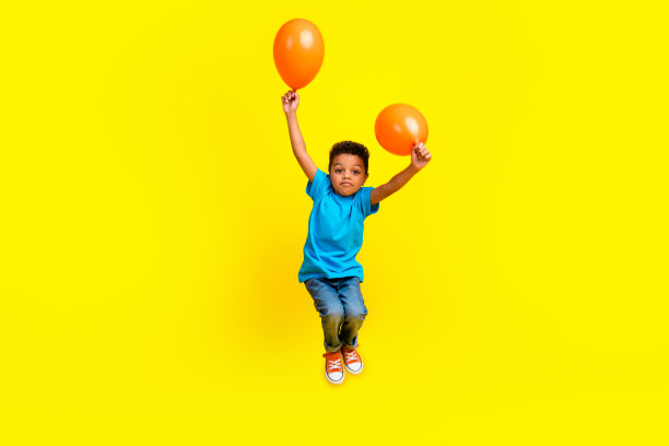 小漂亮孩子的全身照片，穿着蓝色t恤牛仔裤，在充满活力的黄色背景上飞着氦气泡图片下载