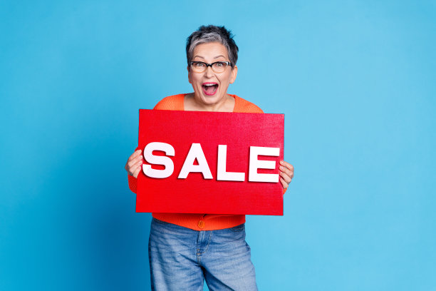 可爱的高级女士的照片肖像拿着销售板横幅惊讶地穿着时尚的橙色服装孤立的蓝色背景图片下载