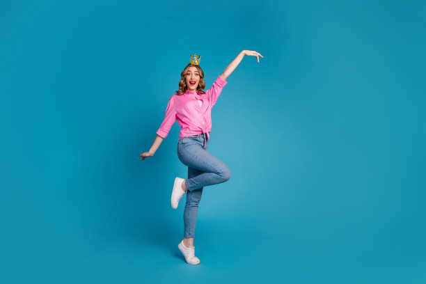 漂亮的年轻女孩的全身照片，金色的皇冠公主跳舞，穿着时髦的粉红色衣服，头发在蓝色背景上孤立图片下载