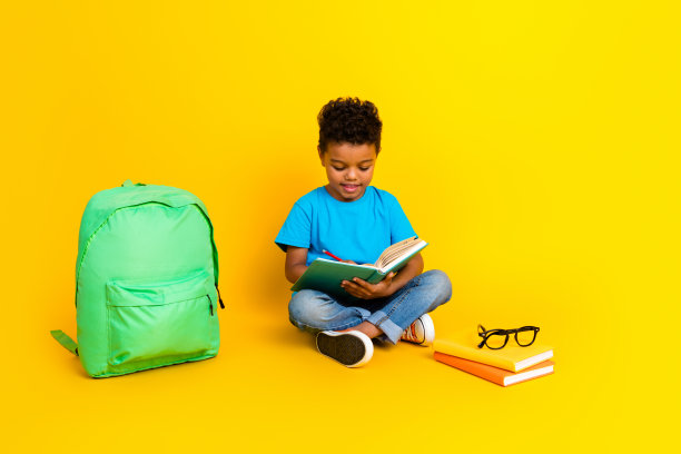 全长照片积极迷人的青春期前的男孩穿蓝色t恤阅读有趣的书孤立的黄色背景图片下载