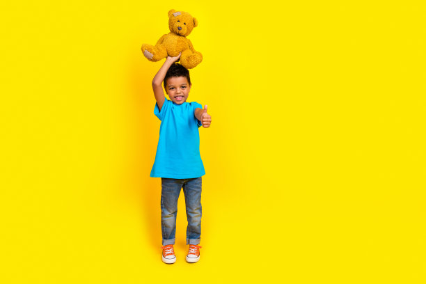 穿着蓝色t恤牛仔裤的多民族多民族儿童的全身照片，头顶上的泰迪熊被隔离在黄色背景上图片下载