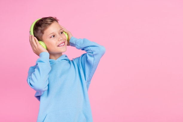 照片积极的小男孩的手臂触摸耳机看起来空的空间想象孤立在粉红色的背景图片下载