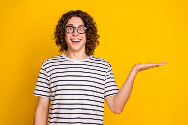 照片肖像漂亮的青少年男性手掌握空的空间广告牌穿时髦的条纹装孤立的黄色背景图片下载