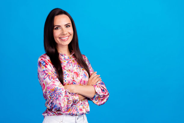 照片中自信可爱的女士穿着印花衬衫，双臂折叠，空白空间孤立的蓝色背景图片下载