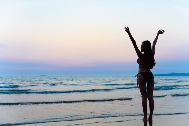 年轻美丽的亚洲女人的剪影照片与比基尼走在美丽的海滩在黄昏日落时间。快乐或自由女人的概念。图片下载