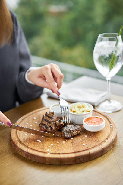 在一家餐馆吃午饭，一位女士吃着烤架上烤好的肝片。在木板上工作的烧烤店的菜单上，有一系列不同肉类的照片。图片下载