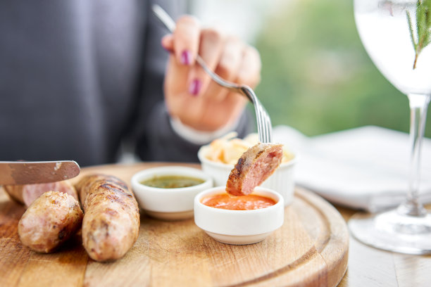 一片香肠蘸着酱汁。在一家餐馆吃午饭，一个女人在切烤香肠。烧烤餐厅的菜单，一系列不同手段的照片。图片下载