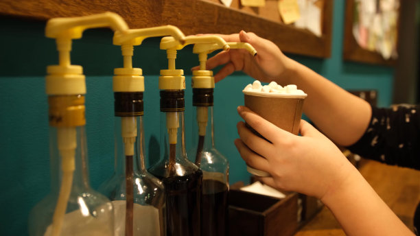 作者咖啡，调酒师在上桌前将焦糖糖浆浇头倒入纸杯中的成品饮料中。模糊的背景图片下载