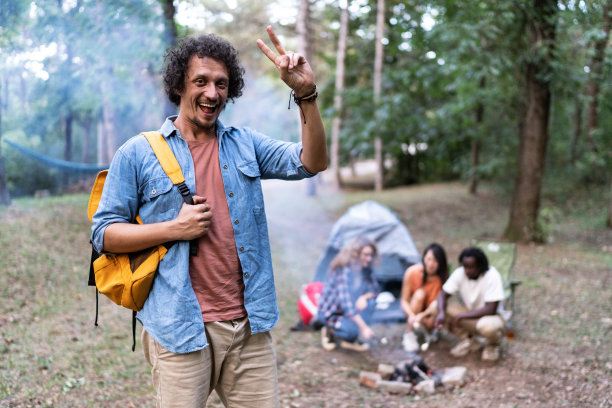 一个微笑着的年轻人和他的朋友们在森林里露营的照片图片下载