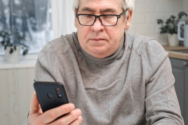 白发苍苍的老人看着网络摄像头，拿着手机，和孩子聊天，老婆上网。老爷爷微笑着与朋友、家人视频聊天。现代科技和老一辈。图片下载