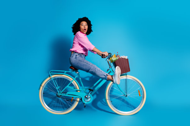 印象深刻的女人穿着粉红色的衬衫骑自行车的全长侧面侧面照片惊讶的凝视孤立在蓝色的背景图片下载