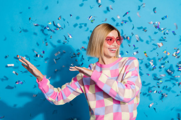 美丽的年轻女孩的照片，太阳眼镜，庆祝派对，跳舞五彩纸屑，穿时髦的粉红色衣服孤立的蓝色背景图片下载