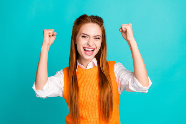 照片中可爱开朗的女孩穿着时髦的橙色服装，举手欢呼，孤立在青色背景上图片下载