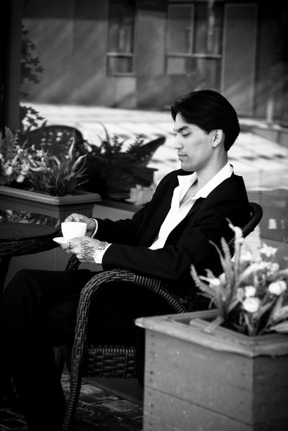 西装革履的亚洲帅哥坐在咖啡馆里喝茶。bw。模糊的照片图片下载