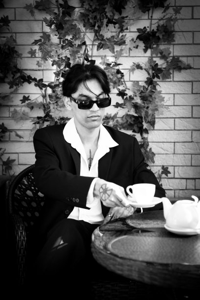 一个西装革履、体贴帅气的亚洲男人坐在咖啡馆里喝茶。bw。模糊的照片图片下载