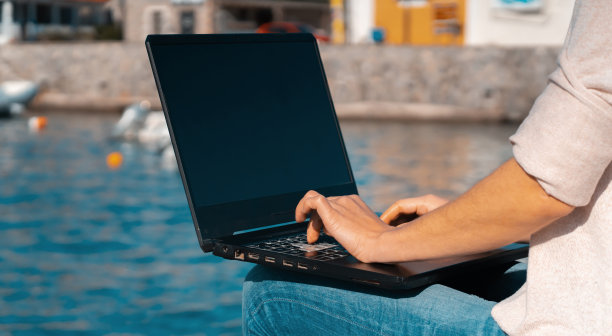 一个女孩正在户外的海边用笔记本电脑键盘打字。图片下载