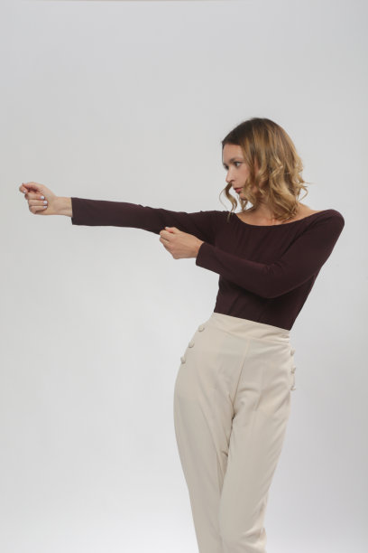 一系列的工作室照片的年轻女模特穿着舒适的基本智能休闲装，酒红色粘胶船领衬衫和米色裤子图片下载