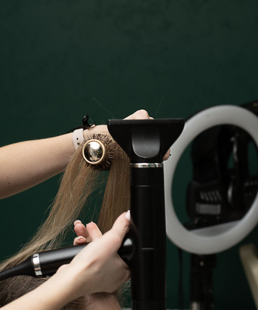 美丽的球体。发型师负责造型和梳头。在美容院，用圆刷为客户梳理长发，然后吹干。特写镜头。经营理念。图片下载