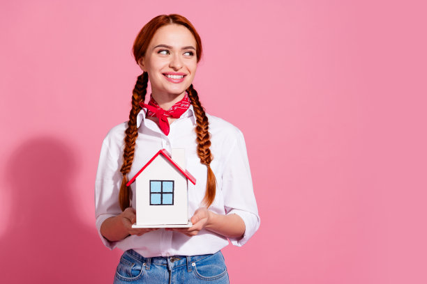 照片中开朗可爱的女孩穿着时髦的衣服，手捧房子看空空间出售新闻孤立在粉红色的背景图片下载