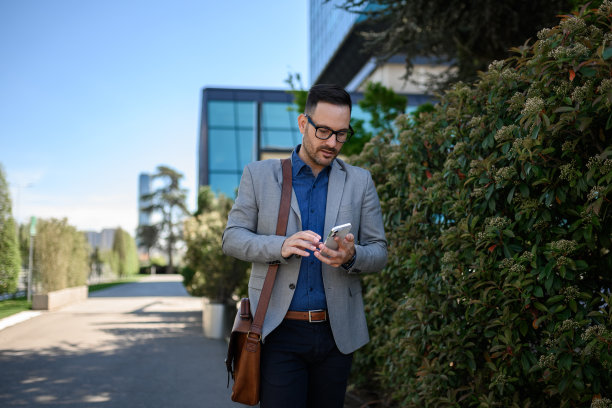 男性商务人士在街上走过植物时用智能手机发短信的照片图片下载