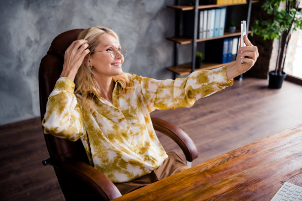 照片肖像可爱的成熟女子拍自拍录像穿着时尚的衬衫办公室白天光家室内工作空间图片下载