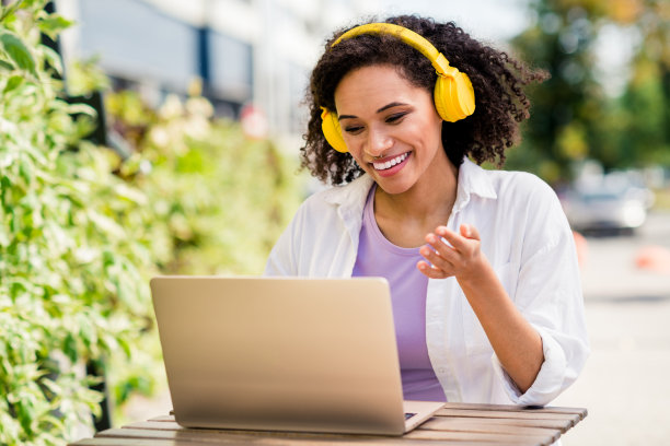 照片中，漂亮闪亮的女士戴着白衬衫耳机，坐在城市公园外的自助餐厅，用现代设备交流图片下载