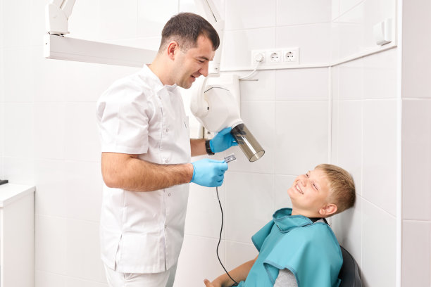 在儿童牙科诊所，放射技师用数字x光机给一个男孩做牙齿x光片。牙医在牙科诊所为小男孩准备牙齿x光照片。图片下载