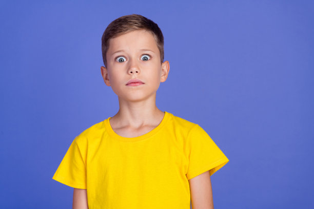 照片中，一个可爱的、担心的、紧张的小男孩穿着时尚的黄色衣服，孤立在紫色的背景上图片下载