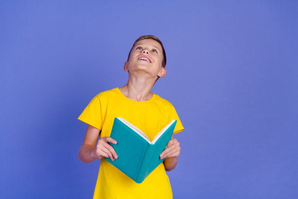 照片中聪明可爱的小男孩书呆子穿着时髦的黄色衣服拿着书规划师在紫色的背景上看起来空无一物图片下载