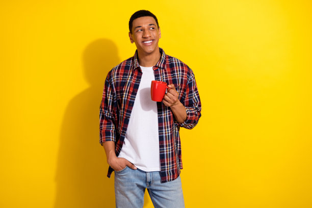 照片中漂亮开朗的男人穿着时髦的衣服，拿着杯子，喝着美味的饮料，在黄色的背景上看起来空无一物图片下载