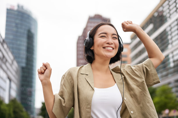 跳舞的亚洲女孩戴着耳机听音乐，在城市里感到快乐，享受户外图片下载