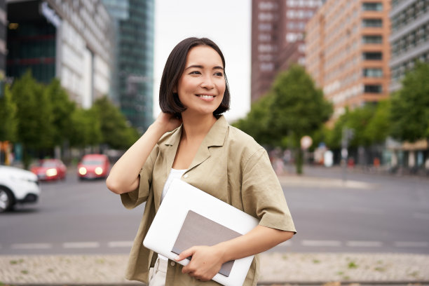 亚洲女孩带着笔记本电脑的户外照片，在市中心的某个地方，走在街上，去上班图片下载