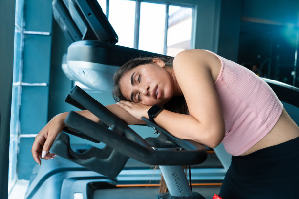 年轻的成年印度妇女在健身房剧烈的有氧运动后在跑步机上睡着了，疲惫的亚洲妇女在健身俱乐部放松肌肉休息，过度训练。图片下载
