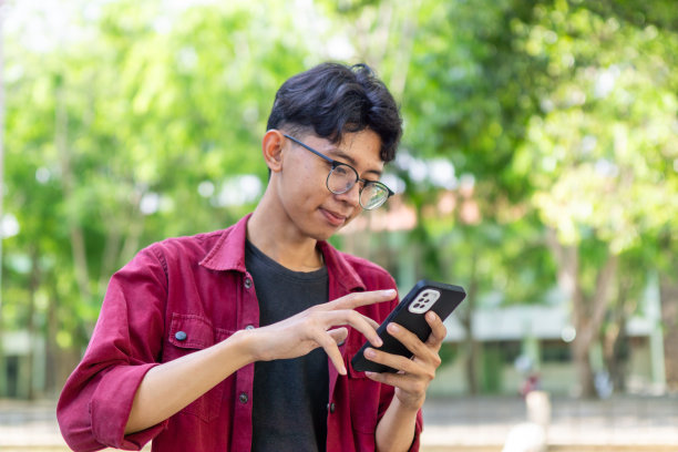 亚洲男子拿着手机微笑的照片。穿着红衬衫的男子一边使用智能手机，一边对着镜头开心地微笑图片下载