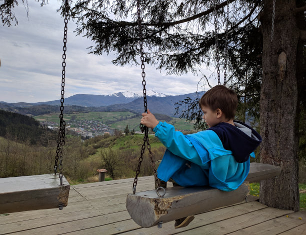 一个男孩骑在秋千上，背景是一个山脉和一个山村，一家人在清新的空气中休闲。照片。图片下载