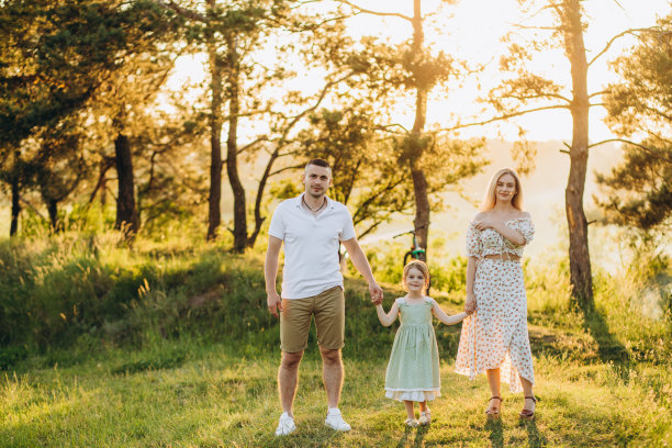 年轻美丽的家庭与一个小女儿拥抱，亲吻和散步在大自然的日落。一个家庭和一个小孩在大自然中的照片。图片下载