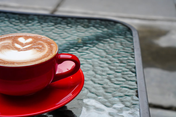 半杯卡布奇诺的照片。用红色杯子盛着的卡布奇诺，放在玻璃桌上图片下载