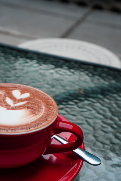 半杯卡布奇诺咖啡。用红色杯子盛着的卡布奇诺，放在玻璃桌上。肖像照片图片下载