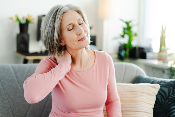 心烦意乱的高级妇女颈部疼痛，坐在家里的沙发上，闭着眼睛。医疗保健理念图片下载