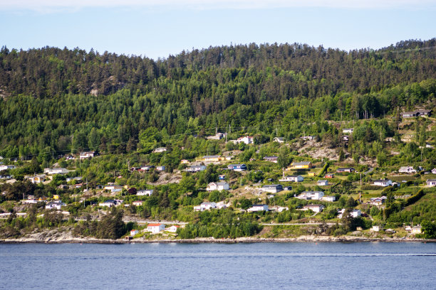 内奥斯陆峡湾，在挪威奥斯陆附近，在一个晴朗的日子里，深蓝色的大海和天空，树木繁茂的山丘和红色屋顶的房子图片下载