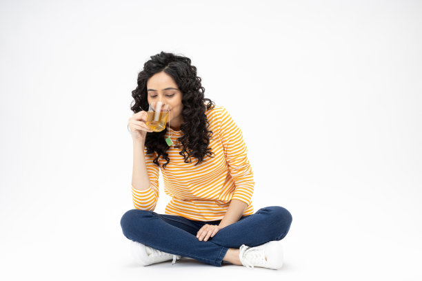 开朗可爱的女人穿着时髦的衣服，坐在地板上喝绿茶，空白的空间孤立在白色背景的照片图片下载