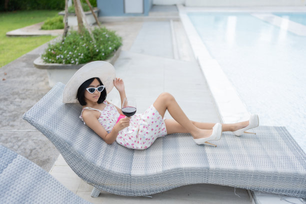 在酒店豪华的环境中，这位年轻的亚洲女子享受着她的假期，优雅地坐在泳池边，手里拿着一杯酒。图片下载