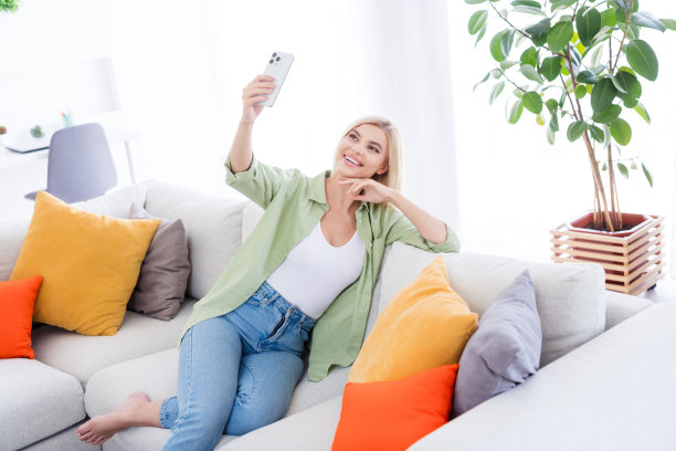 漂亮可爱的开朗女孩坐在自己的公寓沙发上聊天的照片，网络摄像头呼叫流播放白光在室内图片下载