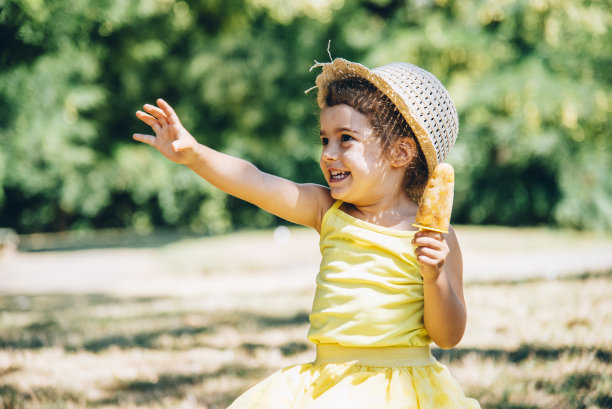 可爱快乐的小女孩穿着黄色的裙子和帽子吃冰淇淋。图片下载
