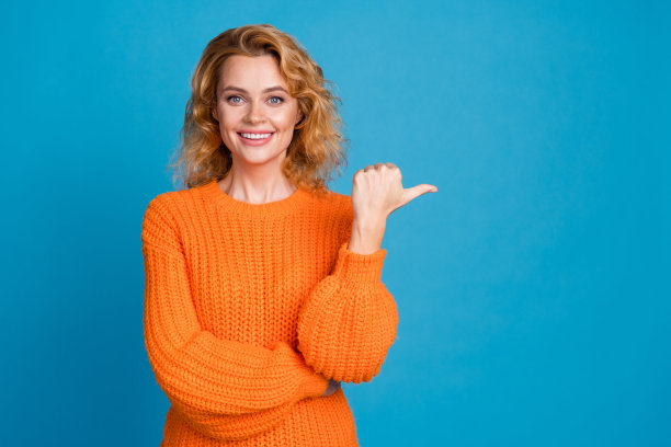 照片满意的可爱的女人穿着时尚的橙色衣服推荐空白空间产品隔离在蓝色背景图片下载