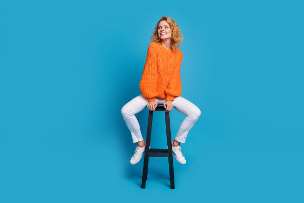 照片令人惊叹的积极华丽的女人穿着时髦的橙色衣服，坐在椅子上，空旷的空间孤立在蓝色的背景图片下载